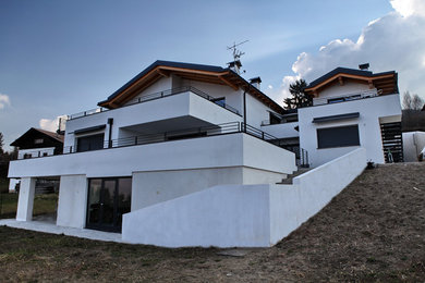 Foto della facciata di una casa bifamiliare bianca contemporanea a piani sfalsati di medie dimensioni con rivestimento in stucco, tetto a capanna e copertura in metallo o lamiera