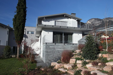 Ejemplo de fachada blanca actual de tamaño medio de tres plantas con revestimiento de piedra, tejado a dos aguas y tejado de teja de barro
