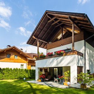 Esempio della villa bianca rustica a tre piani con rivestimento in stucco e tetto a capanna