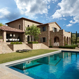 Immagine della facciata di una casa unifamiliare mediterranea a due piani con rivestimento in pietra, tetto a capanna e copertura in tegole
