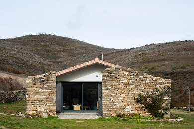 Esempio della facciata di una casa piccola marrone mediterranea a un piano con rivestimento in pietra e tetto a capanna