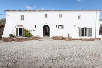 На фото: двухэтажный, белый дом среднего размера в средиземноморском стиле с облицовкой из цементной штукатурки и двускатной крышей