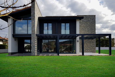 Imagen de fachada de casa moderna de tamaño medio de tres plantas con revestimiento de piedra, tejado a dos aguas y tejado de teja de barro