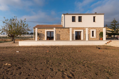 Ejemplo de fachada de casa blanca mediterránea pequeña de dos plantas con revestimientos combinados, tejado a dos aguas y tejado de teja de barro
