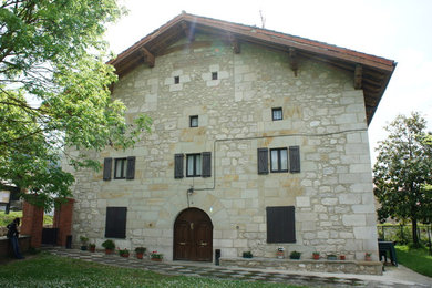 This is an example of a large and gey rustic house exterior in Bilbao with three floors, stone cladding and a pitched roof.