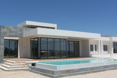 Imagen de fachada de casa gris actual grande de una planta con revestimiento de piedra y tejado plano