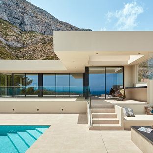Imagen de fachada de casa beige, minimalista, de una planta, con revestimiento de vidrio y tejado plano