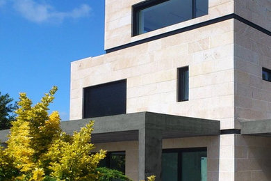 Diseño de fachada de casa beige contemporánea grande de tres plantas con revestimiento de piedra y tejado plano