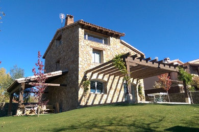 Modelo de fachada beige mediterránea de tamaño medio de tres plantas con revestimiento de piedra y tejado a dos aguas