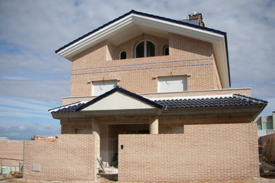 Imagen de fachada de casa roja mediterránea extra grande con revestimiento de ladrillo, tejado a dos aguas y tejado de teja de barro
