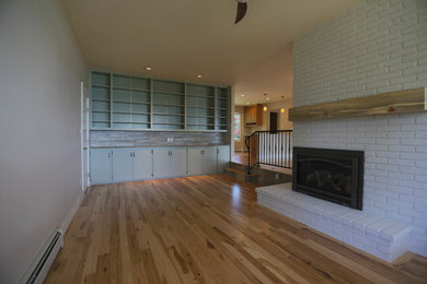 Foto de sala de estar con biblioteca cerrada de estilo americano pequeña con paredes grises, suelo de madera en tonos medios, todas las chimeneas y marco de chimenea de ladrillo