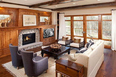 Modelo de sala de estar clásica con paredes beige, suelo de madera oscura, todas las chimeneas, marco de chimenea de piedra y pared multimedia
