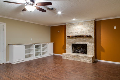 ヒューストンにあるお手頃価格の広いトラディショナルスタイルのおしゃれなオープンリビング (ライブラリー、オレンジの壁、磁器タイルの床、標準型暖炉、石材の暖炉まわり、埋込式メディアウォール、茶色い床) の写真