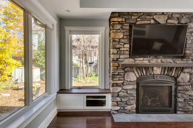 Inspiration for a mid-sized timeless enclosed dark wood floor family room remodel in Ottawa with gray walls, a standard fireplace, a stone fireplace and a media wall