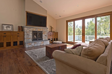 Cette photo montre une grande salle de séjour craftsman ouverte avec un mur beige, parquet foncé, une cheminée standard, un manteau de cheminée en pierre et un téléviseur encastré.