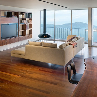 Trendy open concept medium tone wood floor family room photo in San Francisco with white walls, a hanging fireplace and a media wall