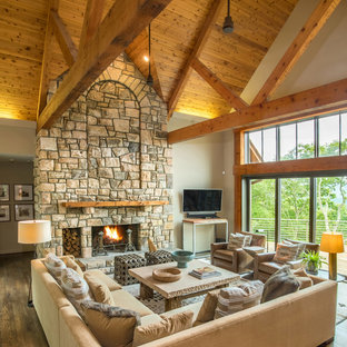 Inspiration for a large rustic open concept brown floor and medium tone wood floor family room remodel in Charlotte with beige walls, a standard fireplace, a stone fireplace and a wall-mounted tv