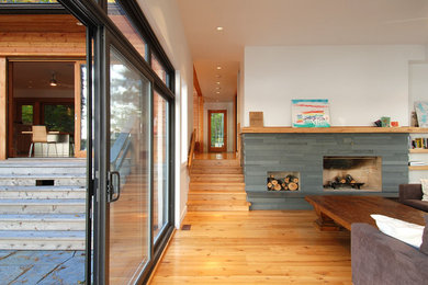 Diseño de sala de estar abierta contemporánea de tamaño medio con paredes blancas, suelo de madera clara, chimenea lineal y marco de chimenea de piedra