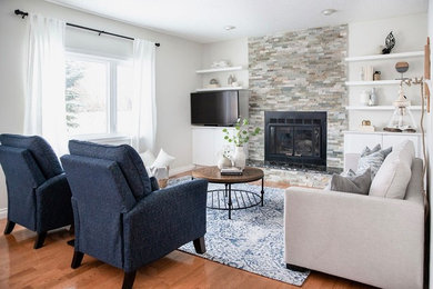 Photo of a medium sized traditional open plan games room in Calgary with grey walls, medium hardwood flooring, a standard fireplace, a stone fireplace surround, a freestanding tv and brown floors.