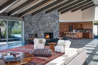 ロサンゼルスにある高級な中くらいなミッドセンチュリースタイルのおしゃれなオープンリビング (ベージュの壁、スレートの床、標準型暖炉、石材の暖炉まわり、グレーの床) の写真