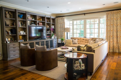 Example of a large classic open concept medium tone wood floor and brown floor family room design in Los Angeles with white walls and a media wall