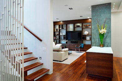 Imagen de sala de estar abierta actual de tamaño medio con paredes blancas, suelo de madera en tonos medios y pared multimedia