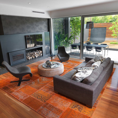 Inspiration for a large contemporary open concept medium tone wood floor and orange floor family room remodel in Melbourne with black walls, a wall-mounted tv, a wood stove and a metal fireplace