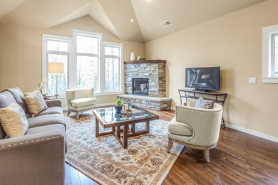 Foto de sala de estar tradicional renovada con paredes beige, suelo de madera en tonos medios, chimenea de esquina, marco de chimenea de piedra y televisor independiente