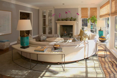 Example of a large 1960s open concept medium tone wood floor family room design in San Diego with gray walls, a standard fireplace, a wood fireplace surround and a concealed tv