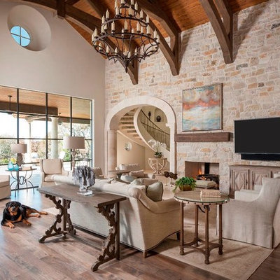 Family room - huge mediterranean open concept light wood floor family room idea in Dallas with white walls, a standard fireplace, a stone fireplace and a wall-mounted tv