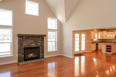 Modelo de sala de estar abierta de estilo americano de tamaño medio con suelo de madera en tonos medios, todas las chimeneas y marco de chimenea de piedra