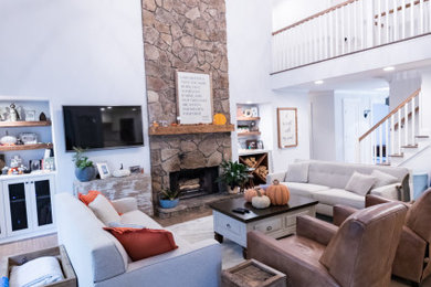 Пример оригинального дизайна: открытая гостиная комната среднего размера в стиле кантри с белыми стенами, паркетным полом среднего тона, стандартным камином, фасадом камина из камня, телевизором на стене и коричневым полом