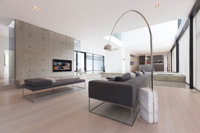 Ejemplo de sala de estar abierta contemporánea grande sin chimenea con paredes blancas, suelo de madera clara, televisor colgado en la pared y suelo beige