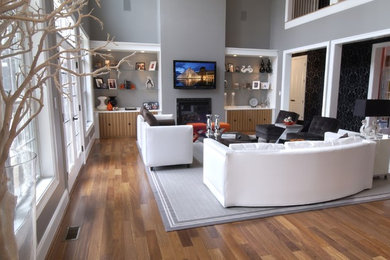 Example of a large trendy medium tone wood floor family room design in Richmond with a standard fireplace and a wall-mounted tv