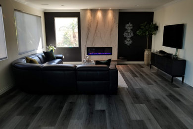 Imagen de sala de estar abierta minimalista con paredes multicolor, suelo vinílico, chimeneas suspendidas, marco de chimenea de piedra y televisor colgado en la pared