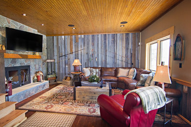 Mountain style dark wood floor living room photo in St Louis with beige walls, a standard fireplace, a stone fireplace and a wall-mounted tv