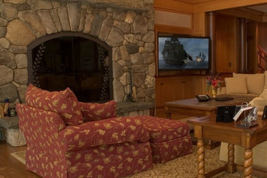 Cette image montre une grande salle de séjour traditionnelle ouverte avec un mur jaune, un sol en bois brun, une cheminée standard, un manteau de cheminée en pierre, un téléviseur encastré, une bibliothèque ou un coin lecture et un sol marron.
