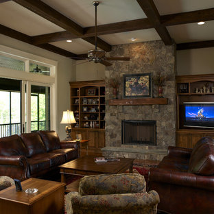 Ejemplo de sala de estar de estilo americano con paredes beige, suelo de madera oscura, chimenea tradicional, marco de chimenea de piedra y pared multimedia