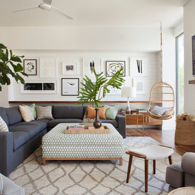 Large beach style open concept medium tone wood floor family room photo in Los Angeles with white walls, a standard fireplace, a plaster fireplace and a wall-mounted tv