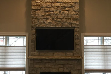 Modelo de sala de estar abierta tradicional pequeña con paredes marrones, moqueta, todas las chimeneas, marco de chimenea de piedra y televisor colgado en la pared