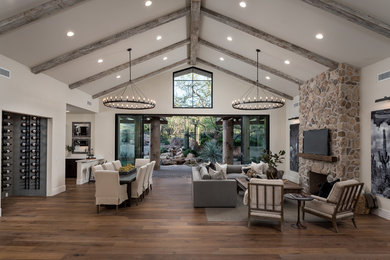 Inspiration for a southwestern open concept brown floor and medium tone wood floor family room remodel in Phoenix with a bar, beige walls, a standard fireplace, a stone fireplace and a wall-mounted tv