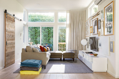 Example of a trendy light wood floor and beige floor family room design in Other with white walls and a wall-mounted tv