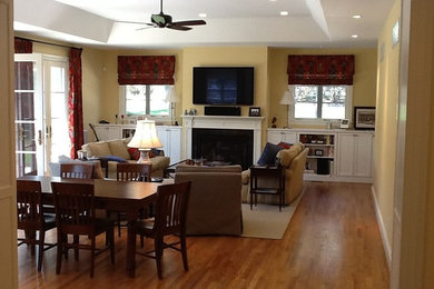 Ejemplo de sala de estar abierta clásica de tamaño medio con paredes amarillas, suelo de madera en tonos medios, todas las chimeneas, marco de chimenea de madera y televisor colgado en la pared