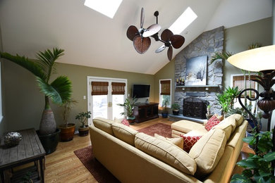 Cette photo montre une salle de séjour chic de taille moyenne et ouverte avec un mur vert, un sol en bois brun, une cheminée standard, un manteau de cheminée en pierre, un téléviseur fixé au mur et un sol marron.