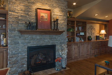 Idée de décoration pour une grande salle de séjour tradition ouverte avec un mur marron, un sol en bois brun, une cheminée standard, un manteau de cheminée en pierre et un téléviseur encastré.
