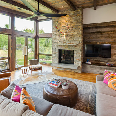 Example of a mountain style medium tone wood floor and brown floor family room design in Denver with white walls, a standard fireplace, a stone fireplace and a wall-mounted tv