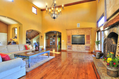 Example of a large tuscan open concept medium tone wood floor family room design in Los Angeles with a stone fireplace and a media wall