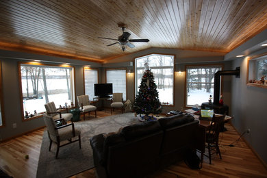 Imagen de sala de estar cerrada tradicional grande con paredes grises, suelo de madera clara, chimenea de esquina y televisor en una esquina