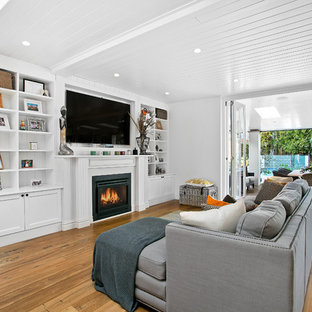 This is an example of a mid-sized transitional open concept family room in Sydney with white walls, dark hardwood floors, a standard fireplace, a wall-mounted tv, a wood fireplace surround and brown floor.