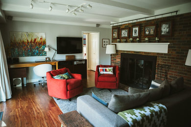 Modelo de sala de estar cerrada clásica renovada de tamaño medio con paredes grises, suelo laminado, todas las chimeneas, marco de chimenea de ladrillo y televisor colgado en la pared